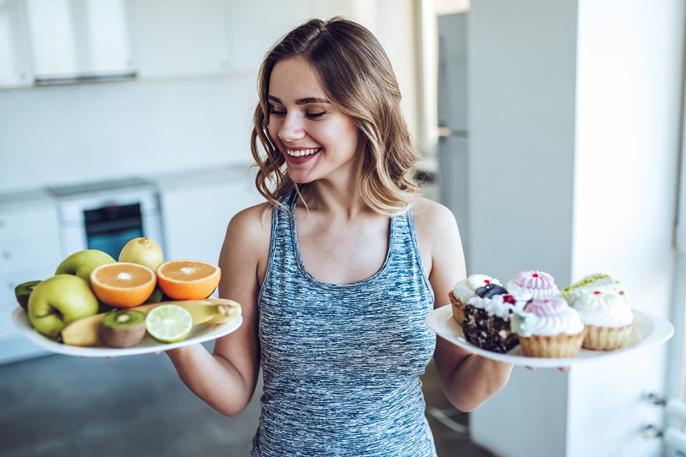 A happy woman looking at the plate full of fruit she's carrying on her right hand while holding a plate full of pastries on her left hand.