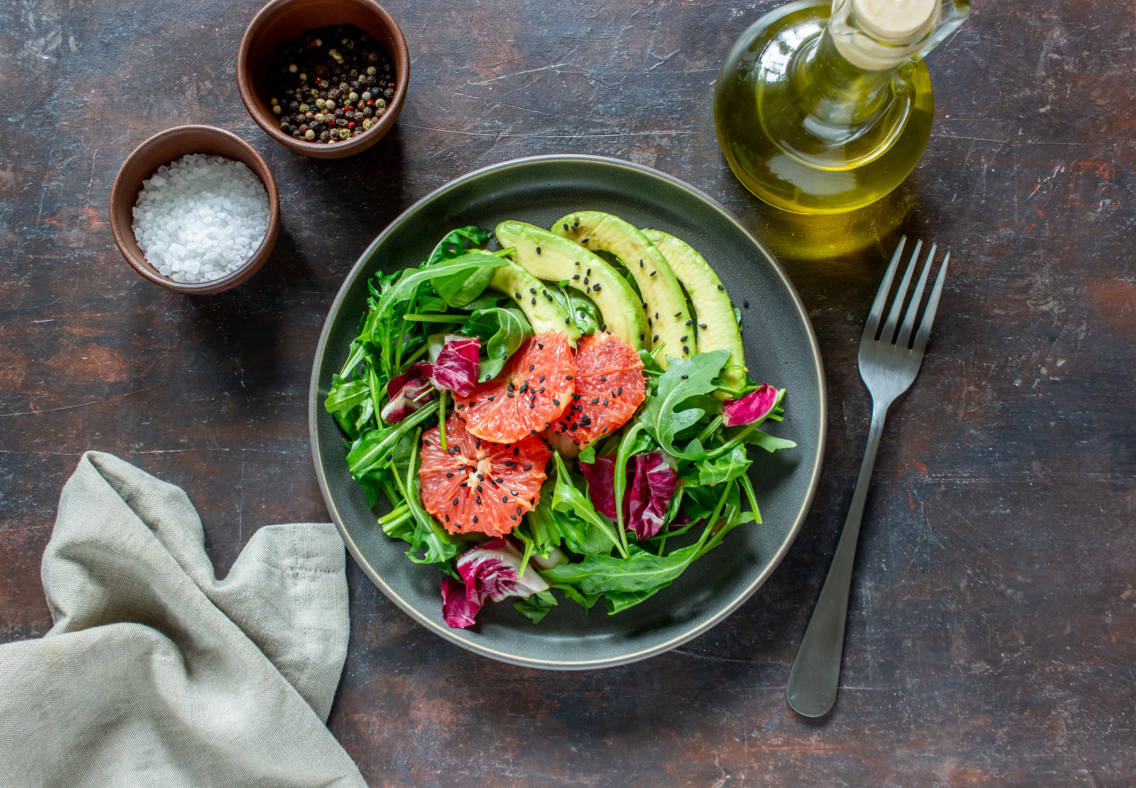 Salad bowl with tomatoes, avocado and arugula on a grey background with oil and vinegar and salt and pepper