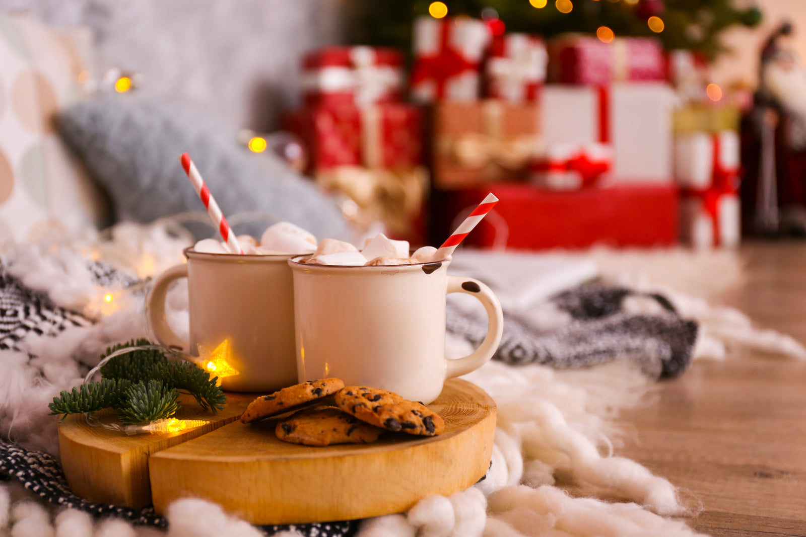 Twin cups of cocoa on a festive holiday background with twinkly lights and presents in the background wrapped in red ribbon