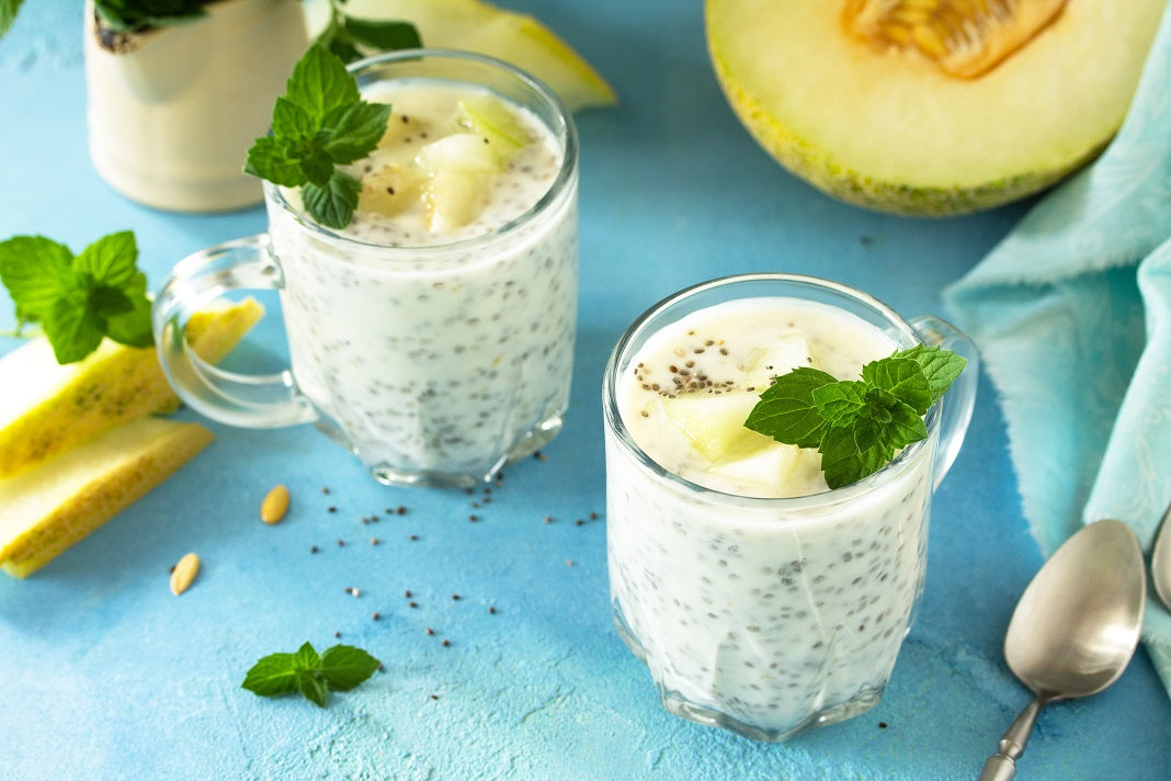 2 glasses of Melon Chia Cleanse with mint leaves next to a tablecloth, tablespoon, and a melon
