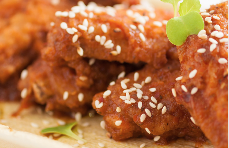 close-up shot of fried chicken wings sprinkled with sesame seeds and green herbs.