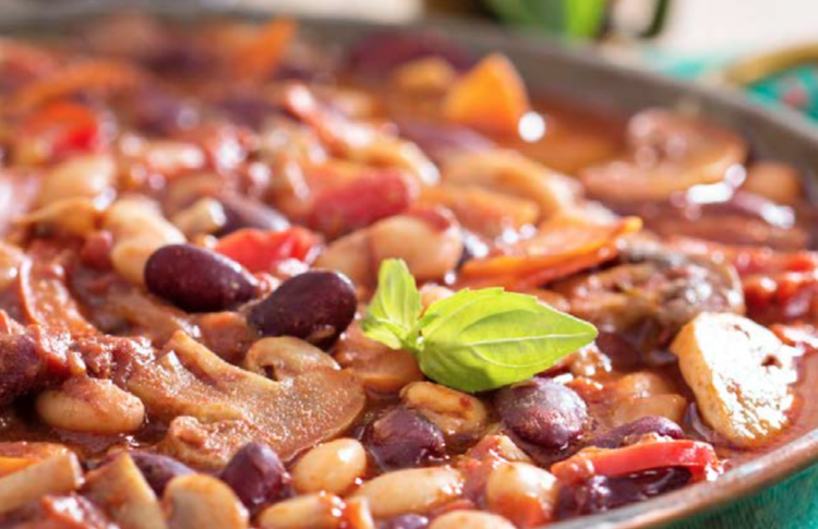 a plate of kidney and black beans with garbanzo and mushrooms in chili sauce with fresh basil on top