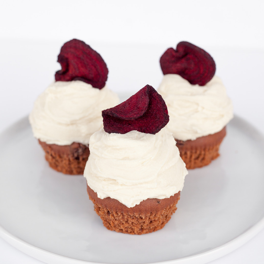 3 cupcakes with white frosting topped with a slice of dried beet root.