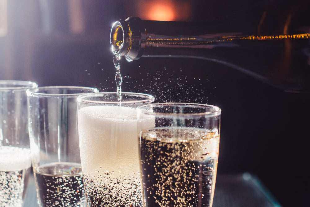 four glasses of green mimosa, two half-full glasses, one full glass, and a brown long neck bottle pouring a green mimosa into a glass