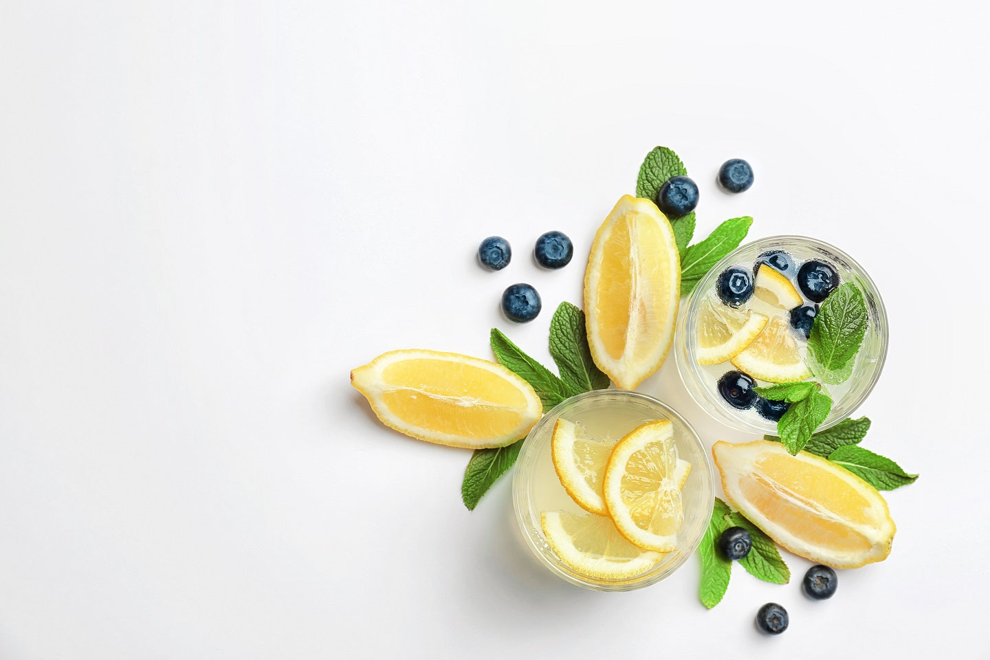 2 glasses of Blueberry Lemon Green Smoothie with slices of lemon, mint, and blue berries surrounded with mint leaves, blueberries and lemon slices