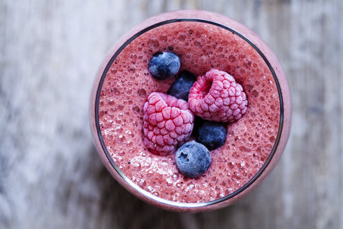 top view of berry apple smoothie topped with blue and red berry placed on top of a wooden table