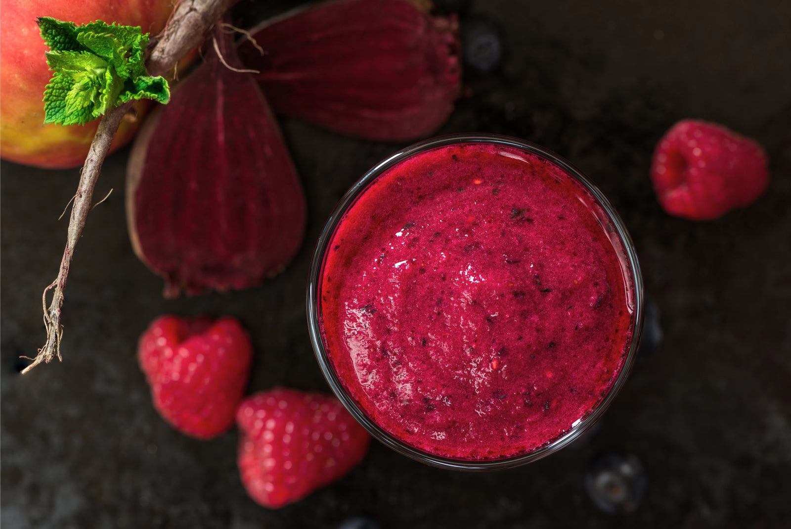 top view shot of a glass of  Cherry-Berry Beets Smoothie beside raspberries and sliced beet roots.