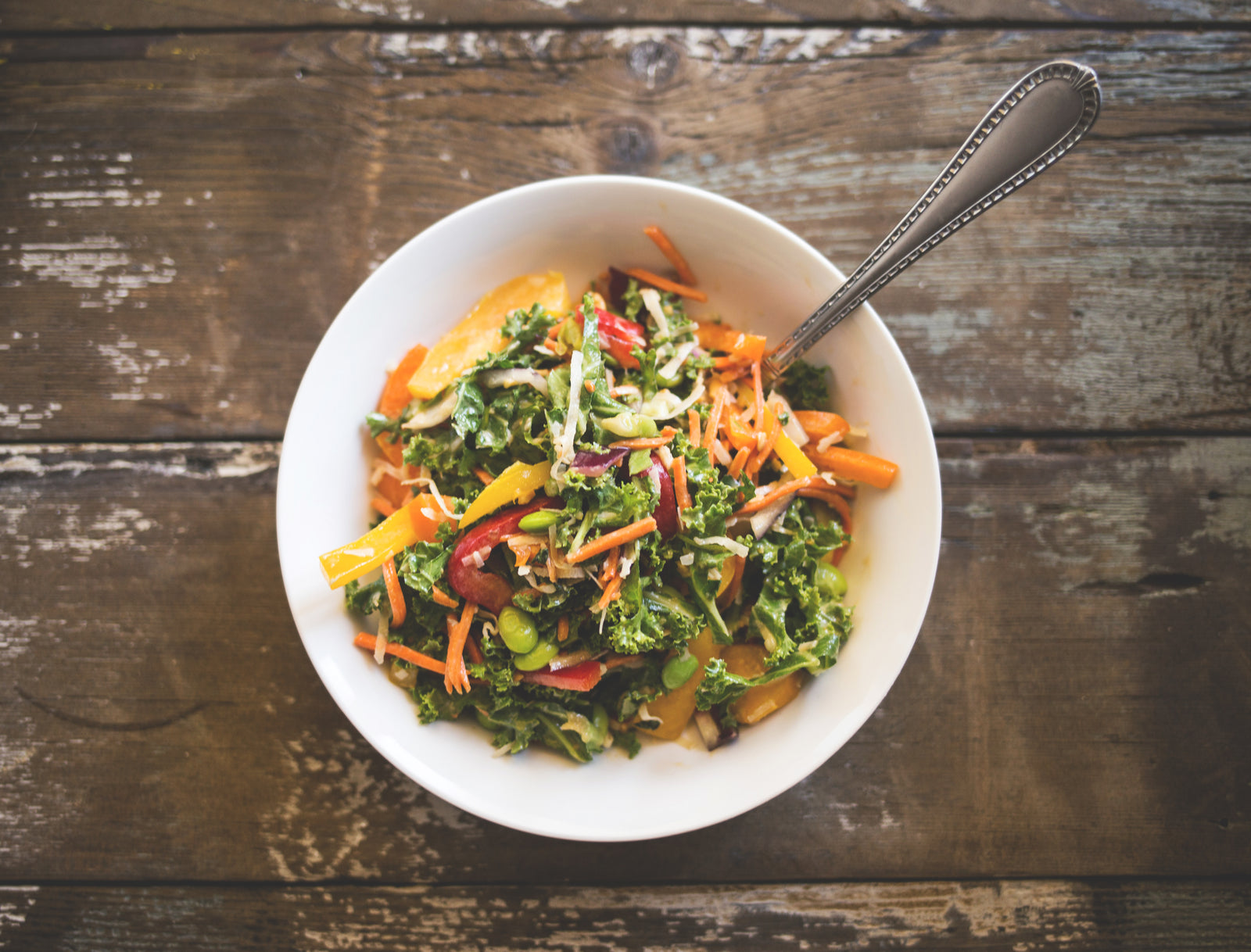 top view of bowl with Asian wild rice & kale salad with citrus-miso dressing with a spoon on top of a wooden table